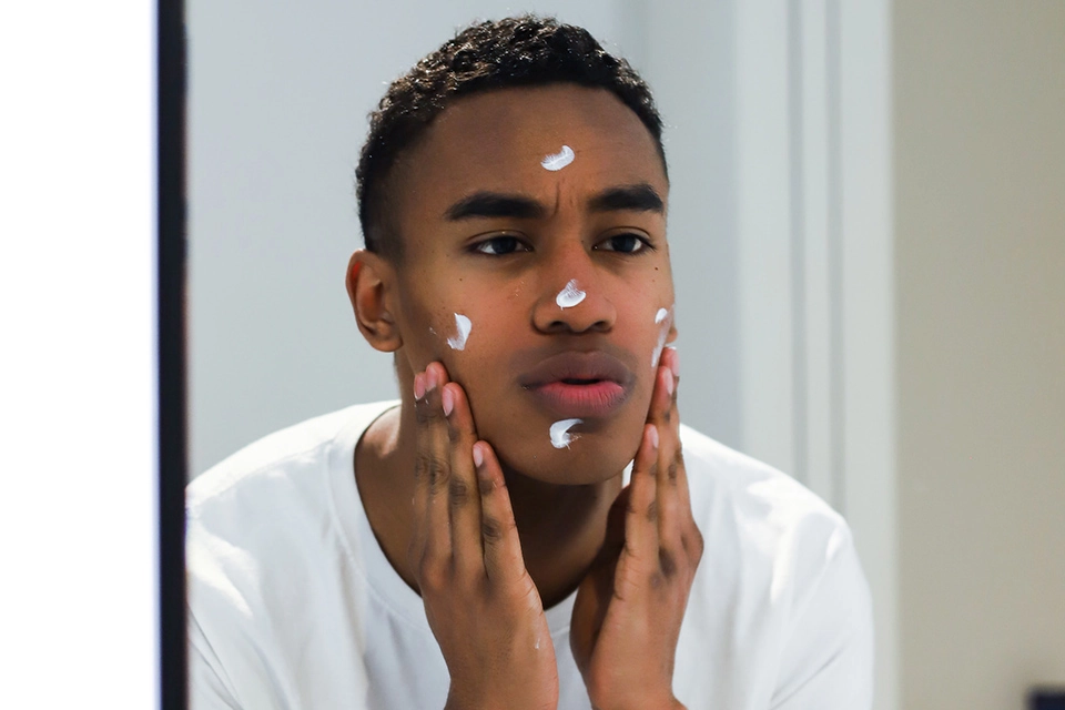 Young man putting on skin cream in a mirror
