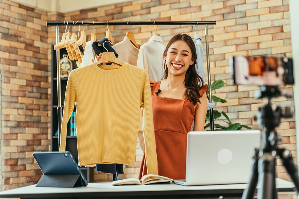 influencer holding up a yellow sweater in front of several other hanging items of clothing